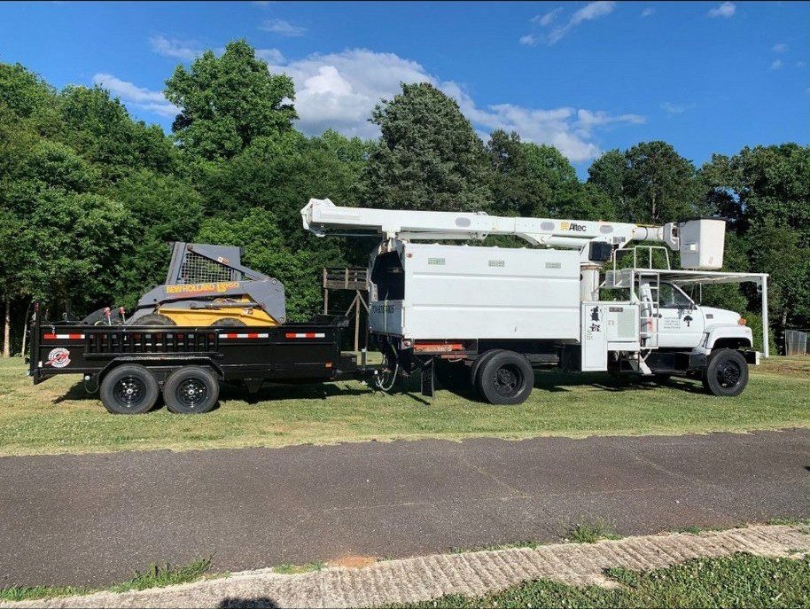 Bucket truck, skid loader, and dump trailer parked together